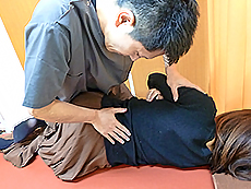 横向きに寝ている患者の肩を押さえながら後ろの腰部を施術するようす
